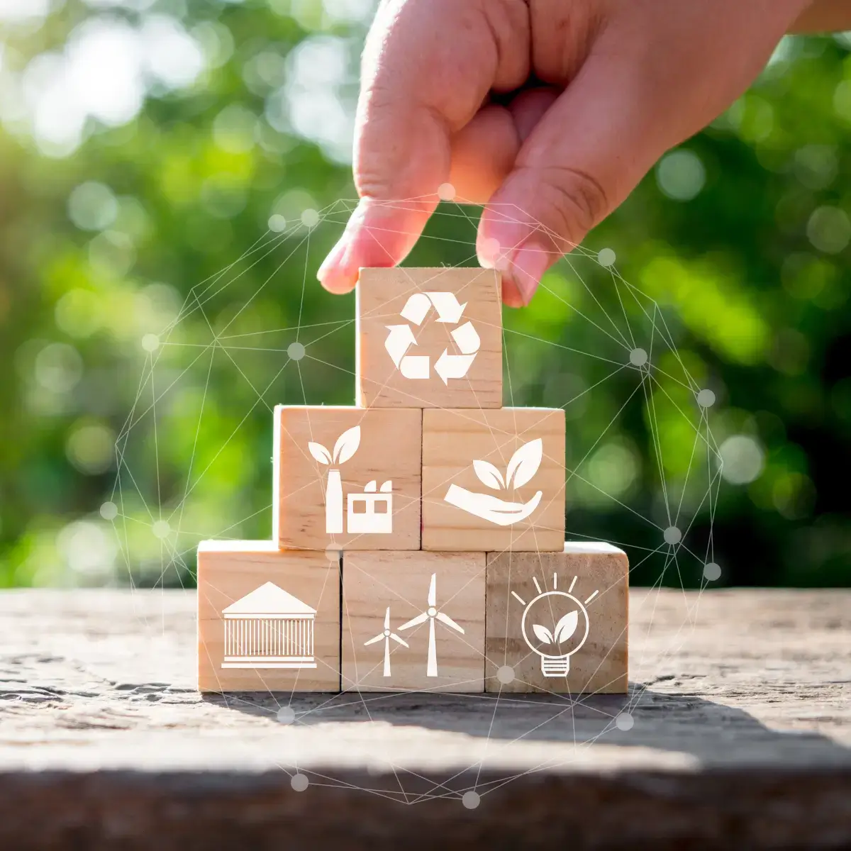 ESG (2) Mão a colocar cubo com símbolo de reciclagem sobre blocos de madeira com ícones sustentáveis conectados em rede