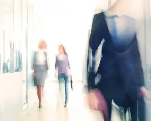 Pessoas em movimento desfocado num corredor de escritório moderno